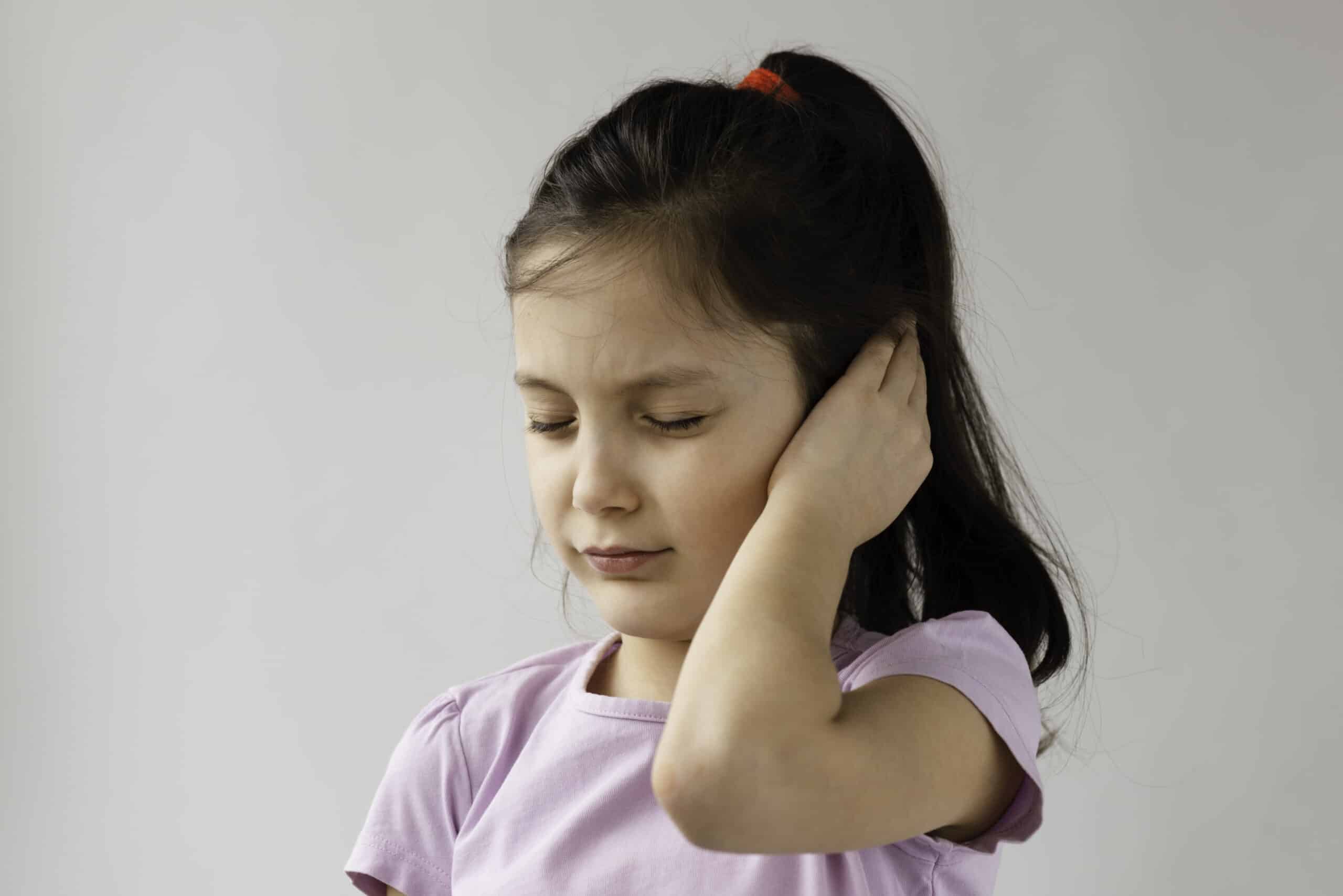 Little girl is holding her ear because of ear pain. Her eyes are closed.