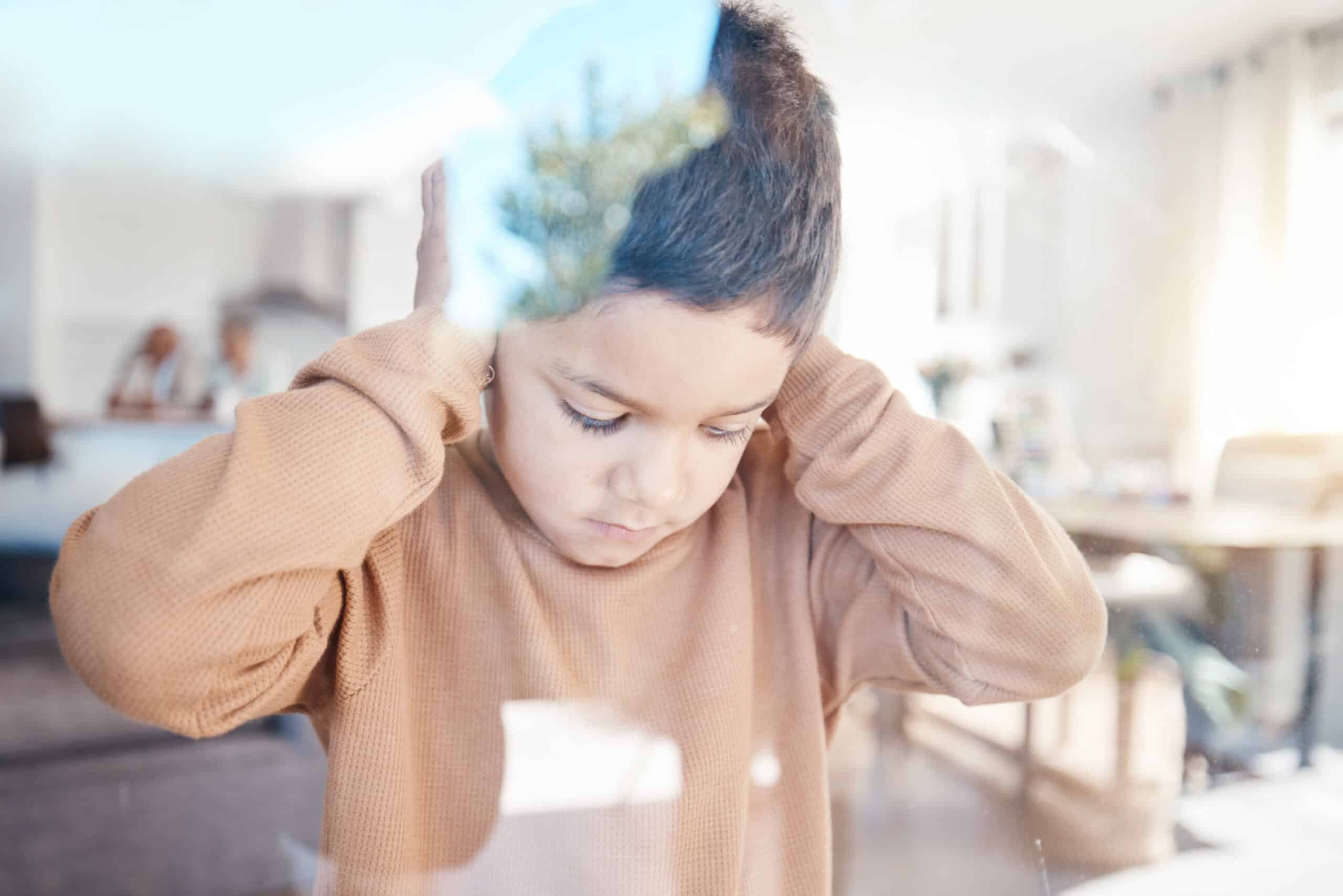 Sad, home and boy with hands on ears for depression, fear and scared of conflict with family by window. Child psychology, autism and depressed, anxiety and upset kid in living room for mental health